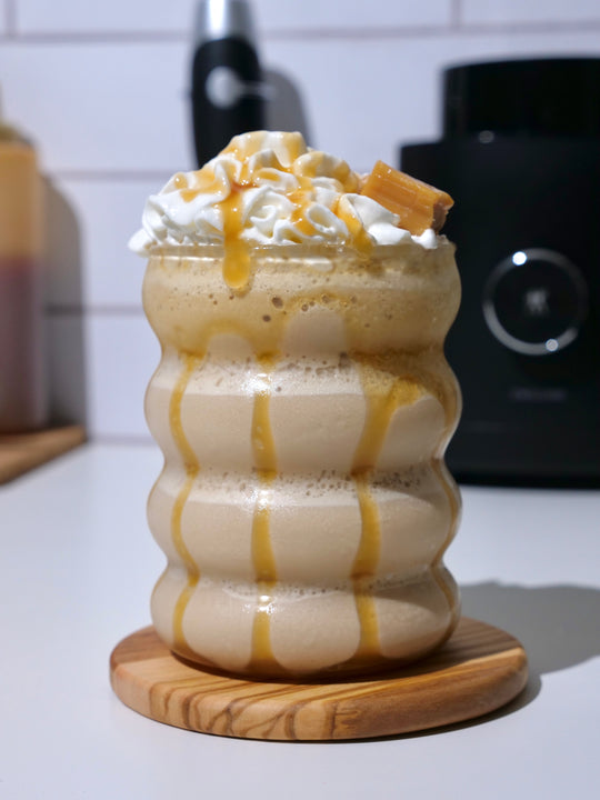 Caramel frappe drink with caramel sauce oozing over edge with a caramel chunk on top served in a modern glass on a counter