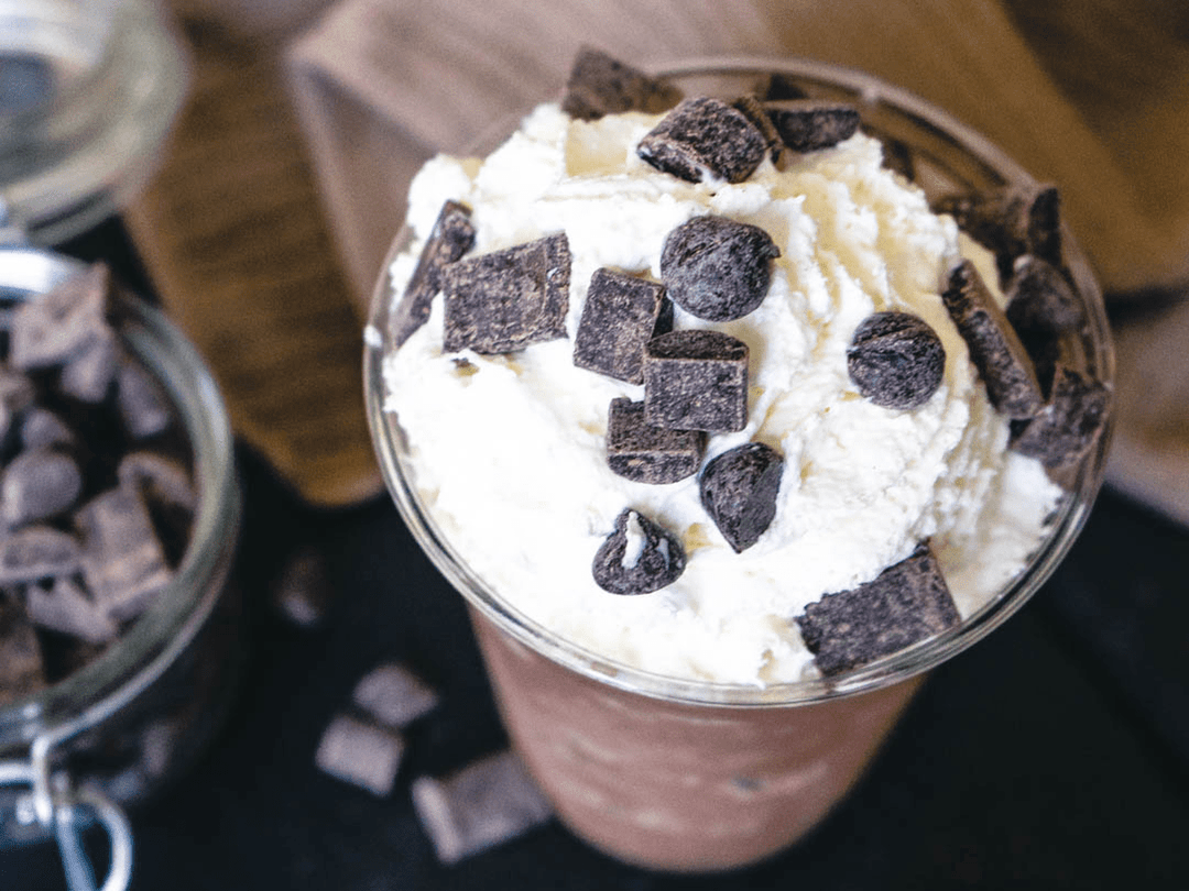 Close up looking down of a Java Chip frappe blended drink topped with whipped cream and chocolate chunks on top.