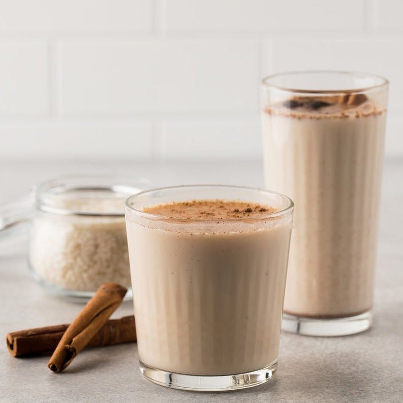 Horchata blended with ice and hot both garnished with powdered cinnamon next to a jar of rice