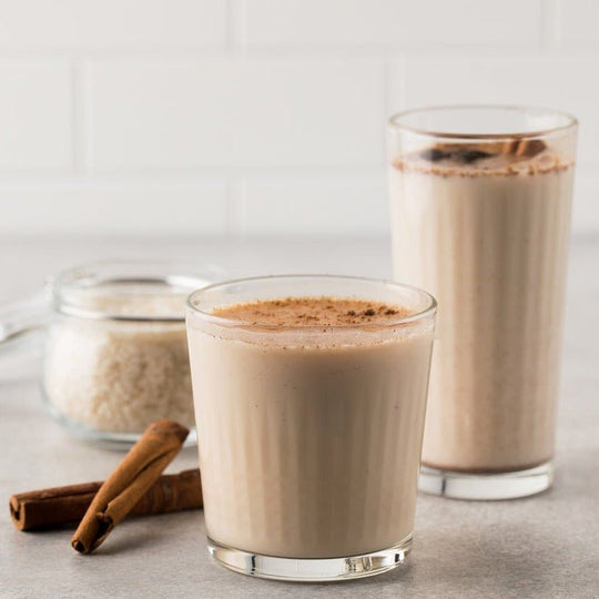 Horchata blended with ice and hot both garnished with powdered cinnamon next to a jar of rice