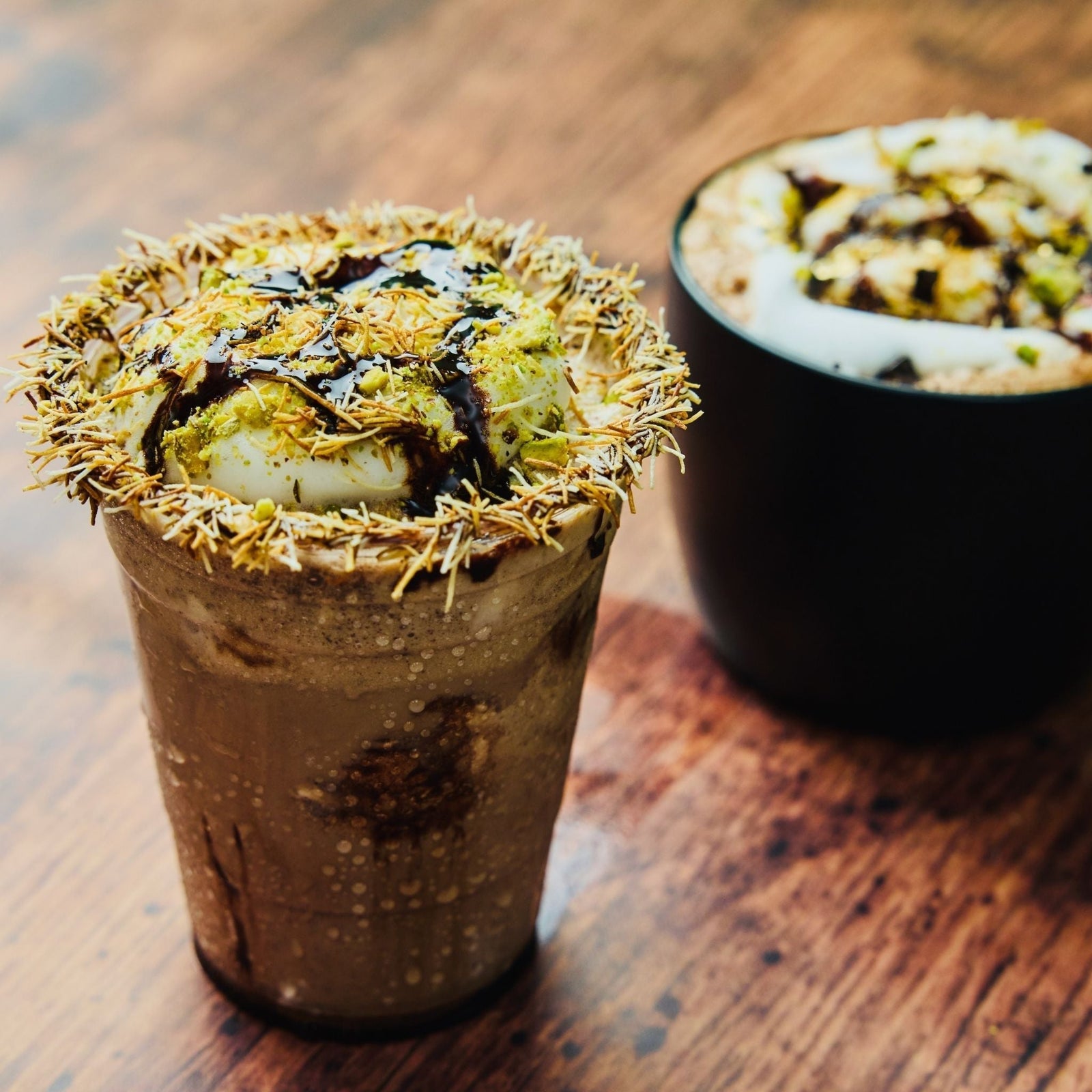 Dubai Chocolate Pistachio Frappe next to a Hot Dubai Chocolate in a black mug 