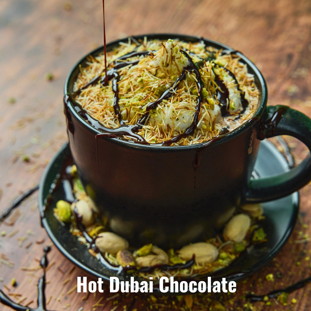 Hot Dubai Chocolate garnished with kataifi, pistachio pieces and chocolate sauce in black mug with shelled pistachios on saucer 